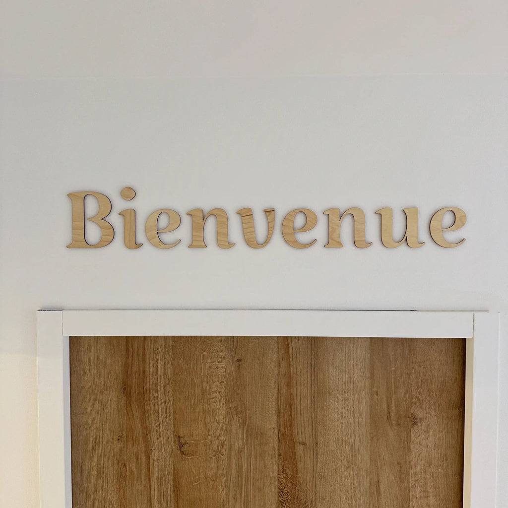 Phrase murale en bois "Bienvenue" accrochée sur un mur blanc