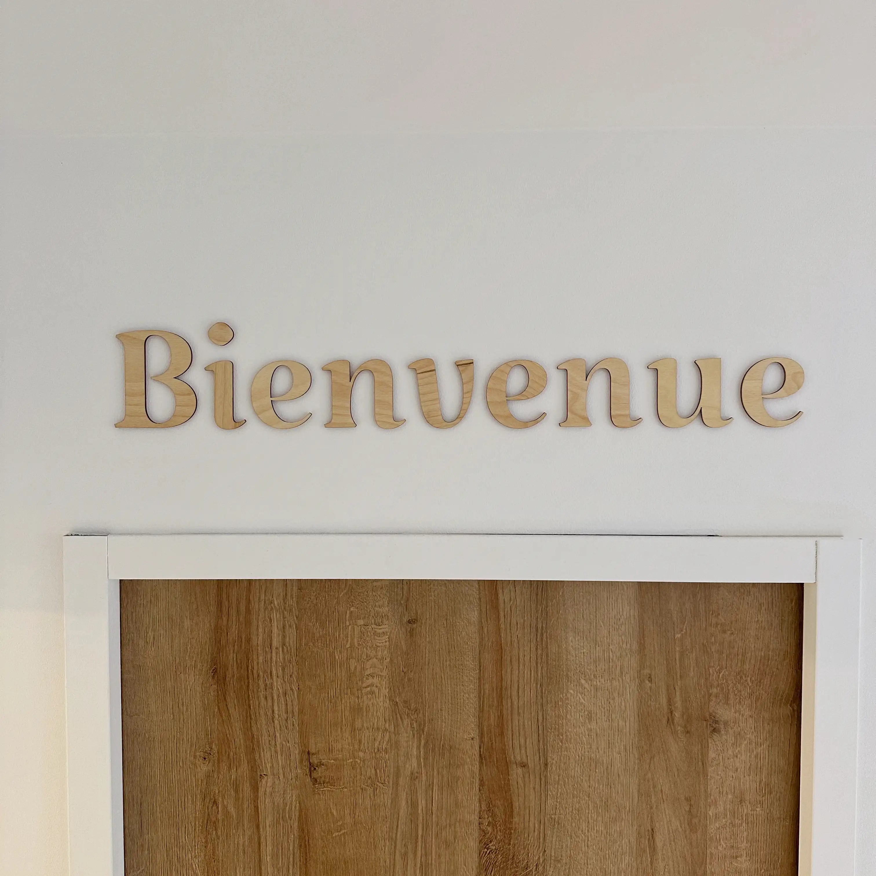 Phrase murale en bois "Bienvenue" accrochée sur un mur blanc