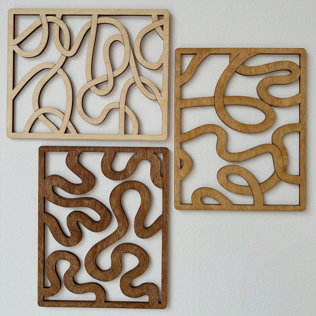 Trois tableaux en bois qui représentent des courbes dans trois coloris distinct, sur mur blanc.