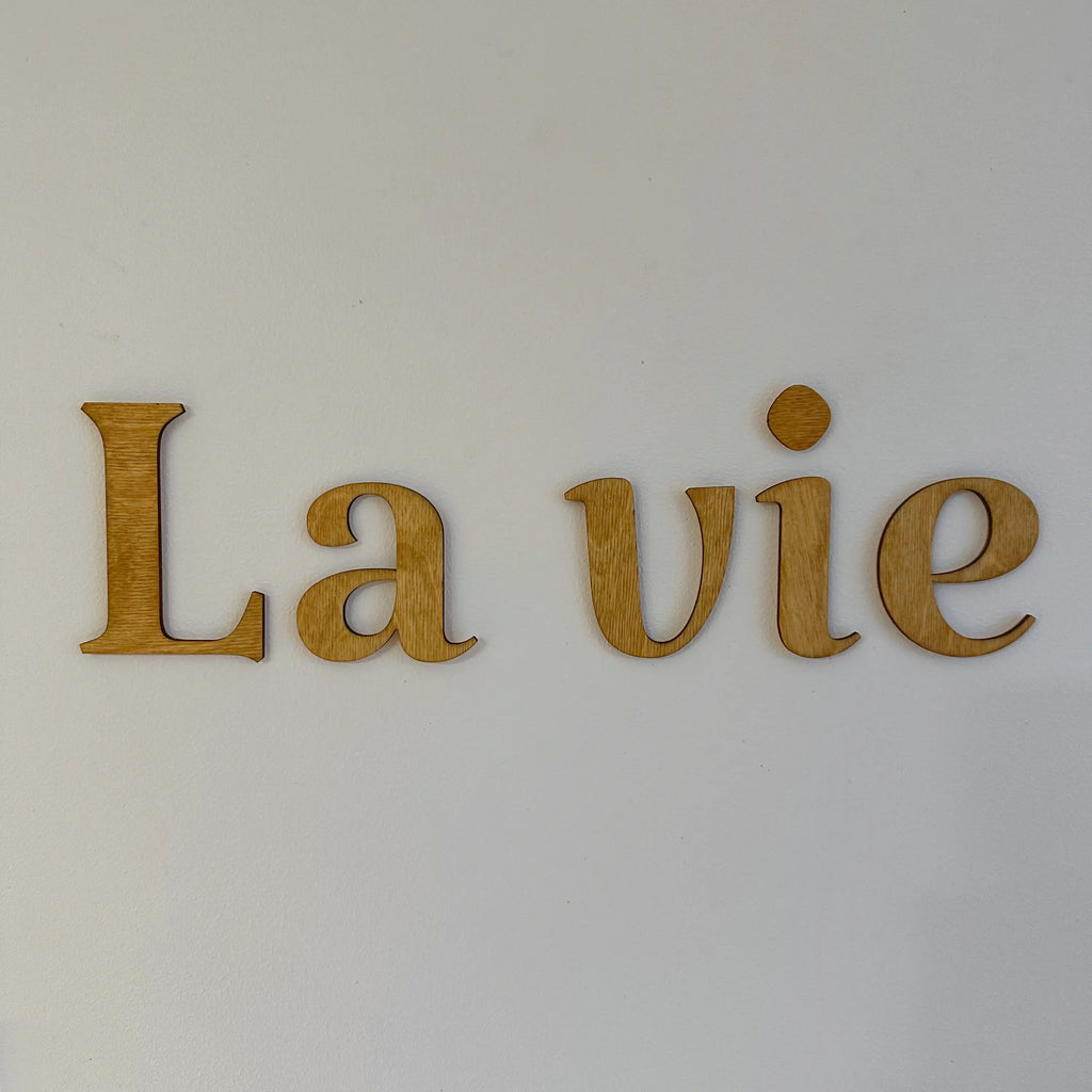 Vue rapprochée sur les mots en bois "La vie" sur un mur blanc