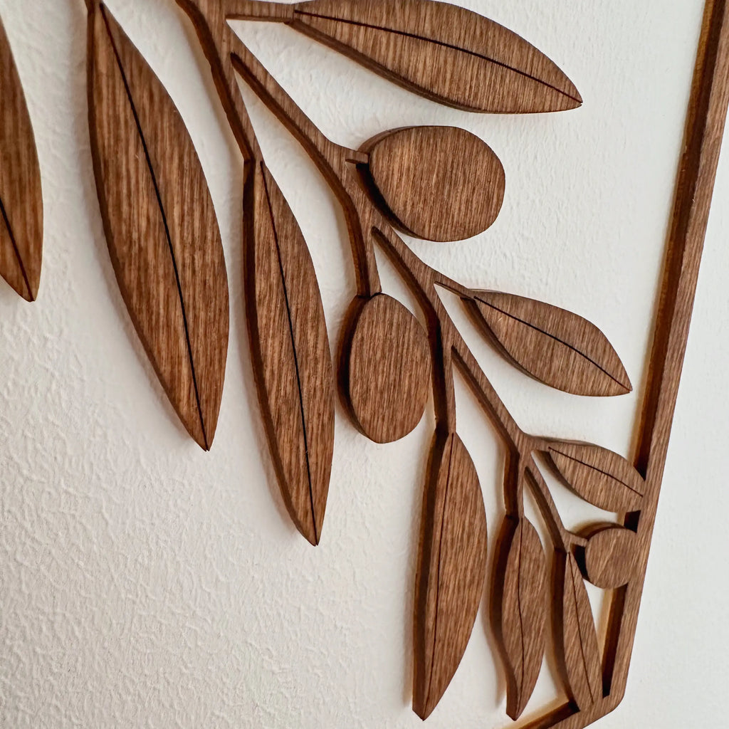 Zoom sur une décoration murale en bois qui représente une branche d'olivier, installé sur un mur de salon.