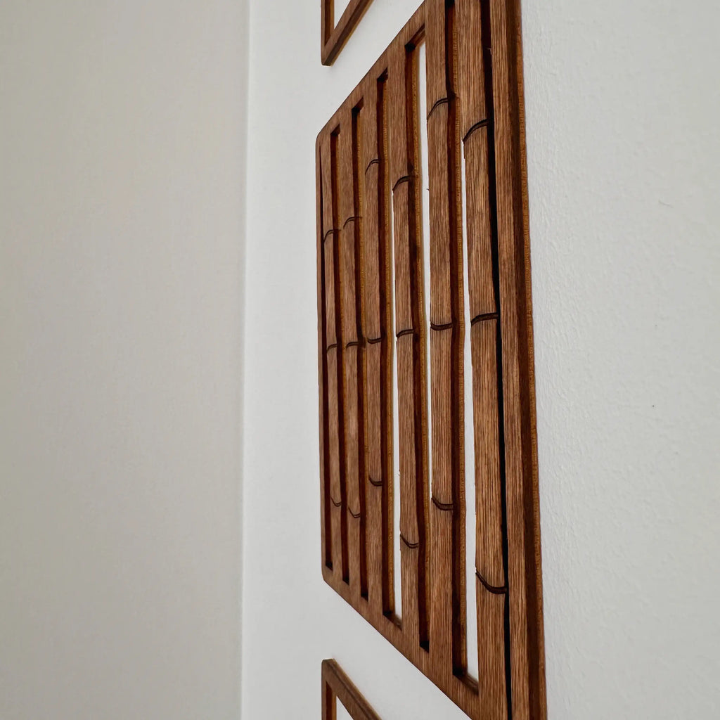 Zoom sur un tableau en bois qui représente une haie de bambou, installé sur un mur blanc.