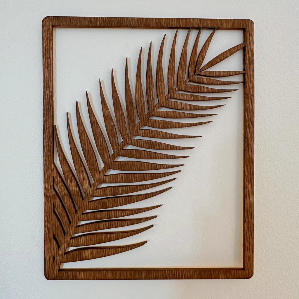Décoration murale qui présente une branche de palmier stylisée dans un cadre en bois.