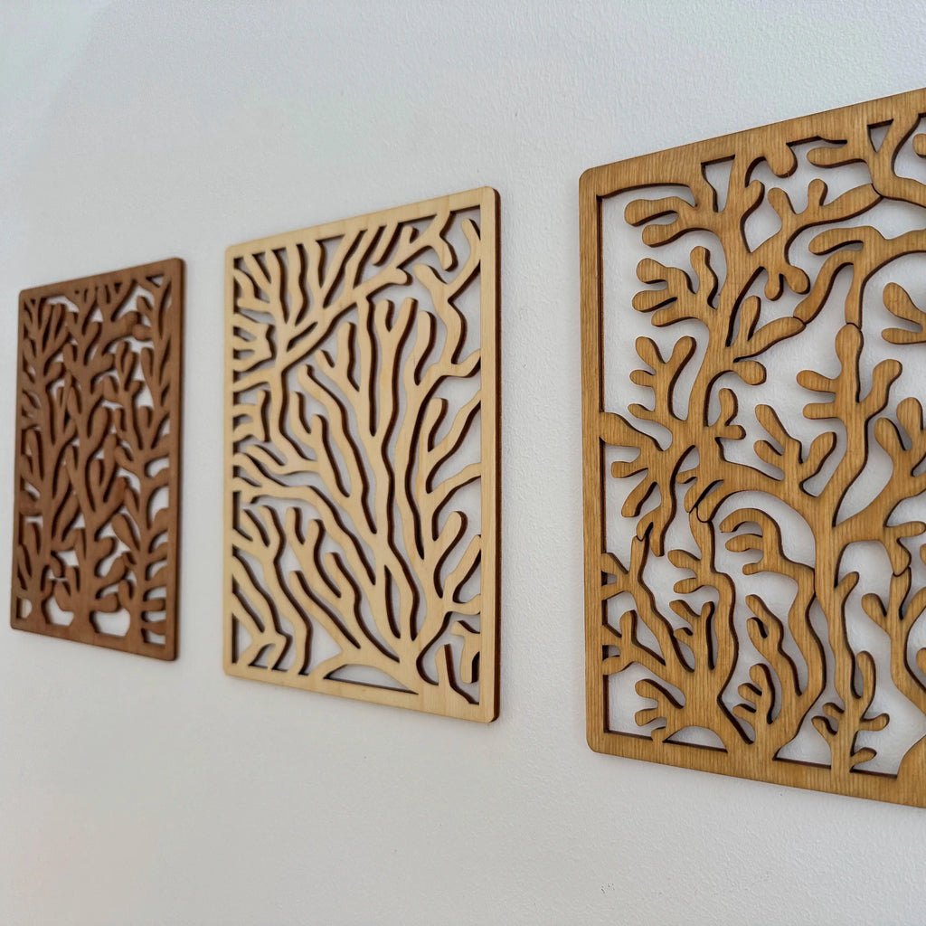 Lot de trois tableaux en bois coraux accrochés sur un mur blanc.