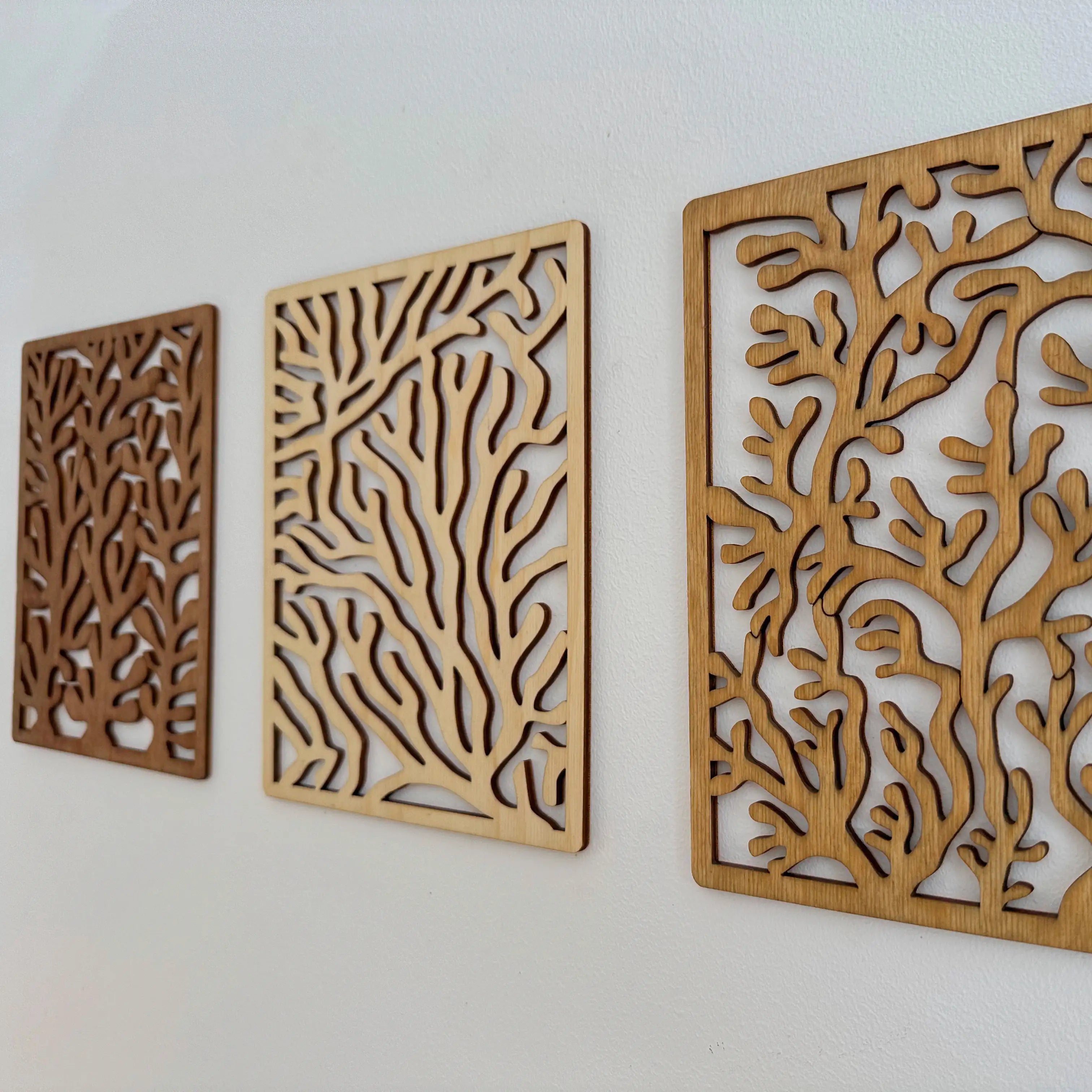 Lot de trois tableaux en bois coraux accrochés sur un mur blanc.