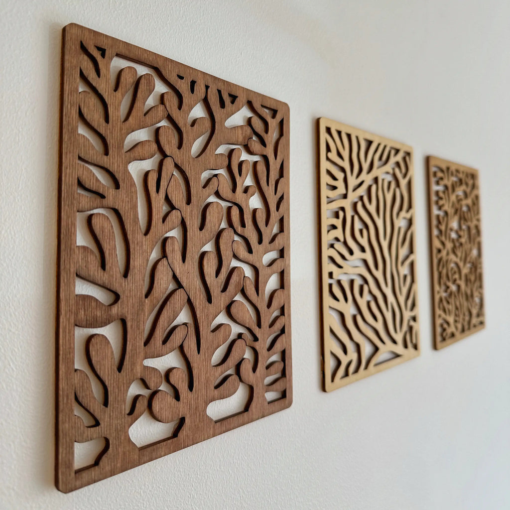 Trois tableaux en bois qui représentent différentes formes de coraux, accrochés sur un mur.
