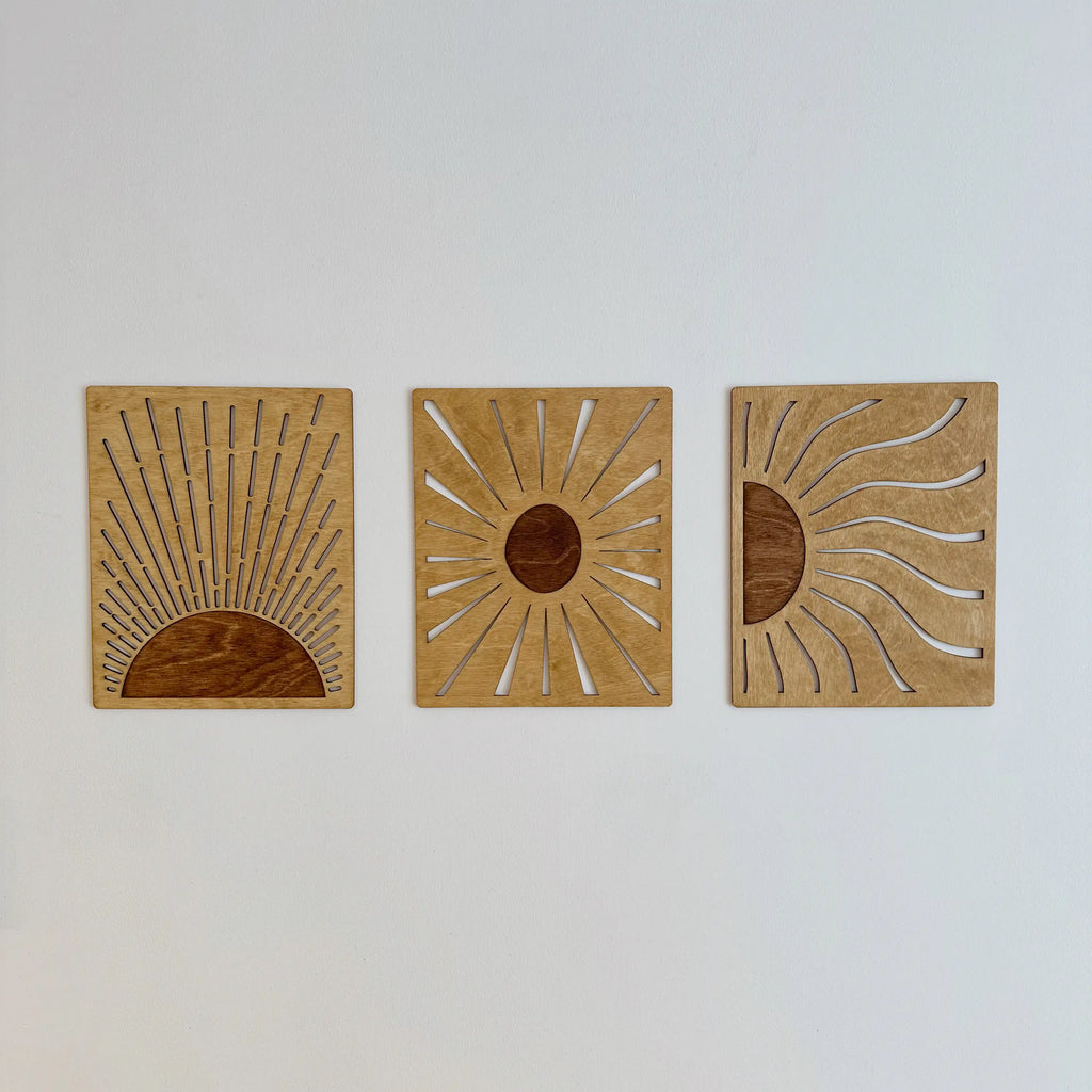 Trois tableaux soleil sur un mur blanc, vue de face, décoration design et chaleureuse.