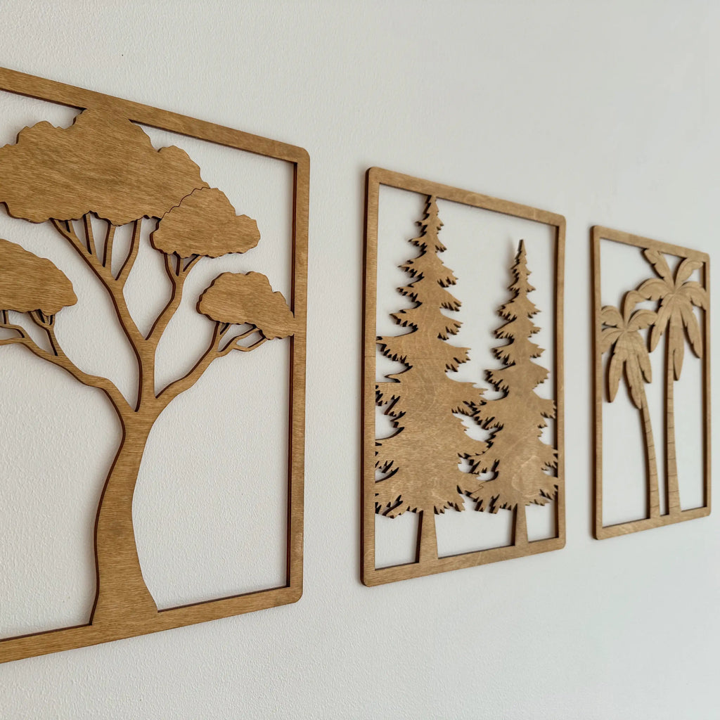 Trois tableaux en bois qui représentent chacun un arbre différent, accrochés sur un mur blanc.